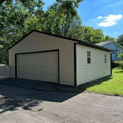 Detached garage with cream siding, dark trim, and a wide door