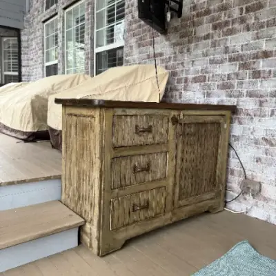 Rustic wood dresser on a covered porch against a brick wall