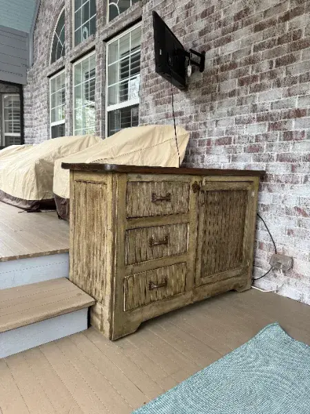 Rustic wood dresser on a covered porch against a brick wall