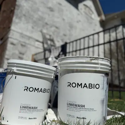 Buckets of Romabio limewash paint in front of a stone house